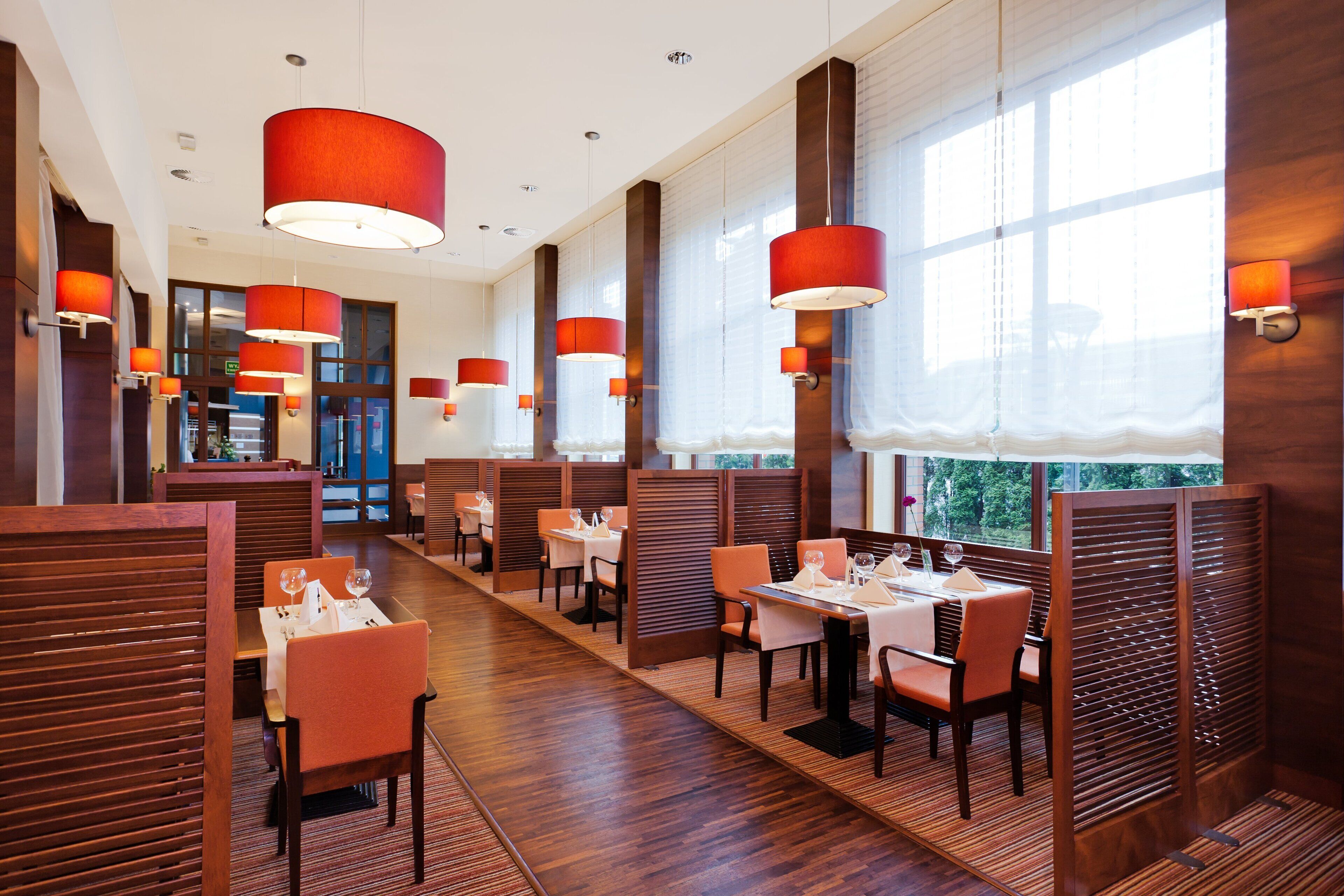 A modern restaurant with wooden panel dividers, red pendant lighting, and a view of the outdoors.