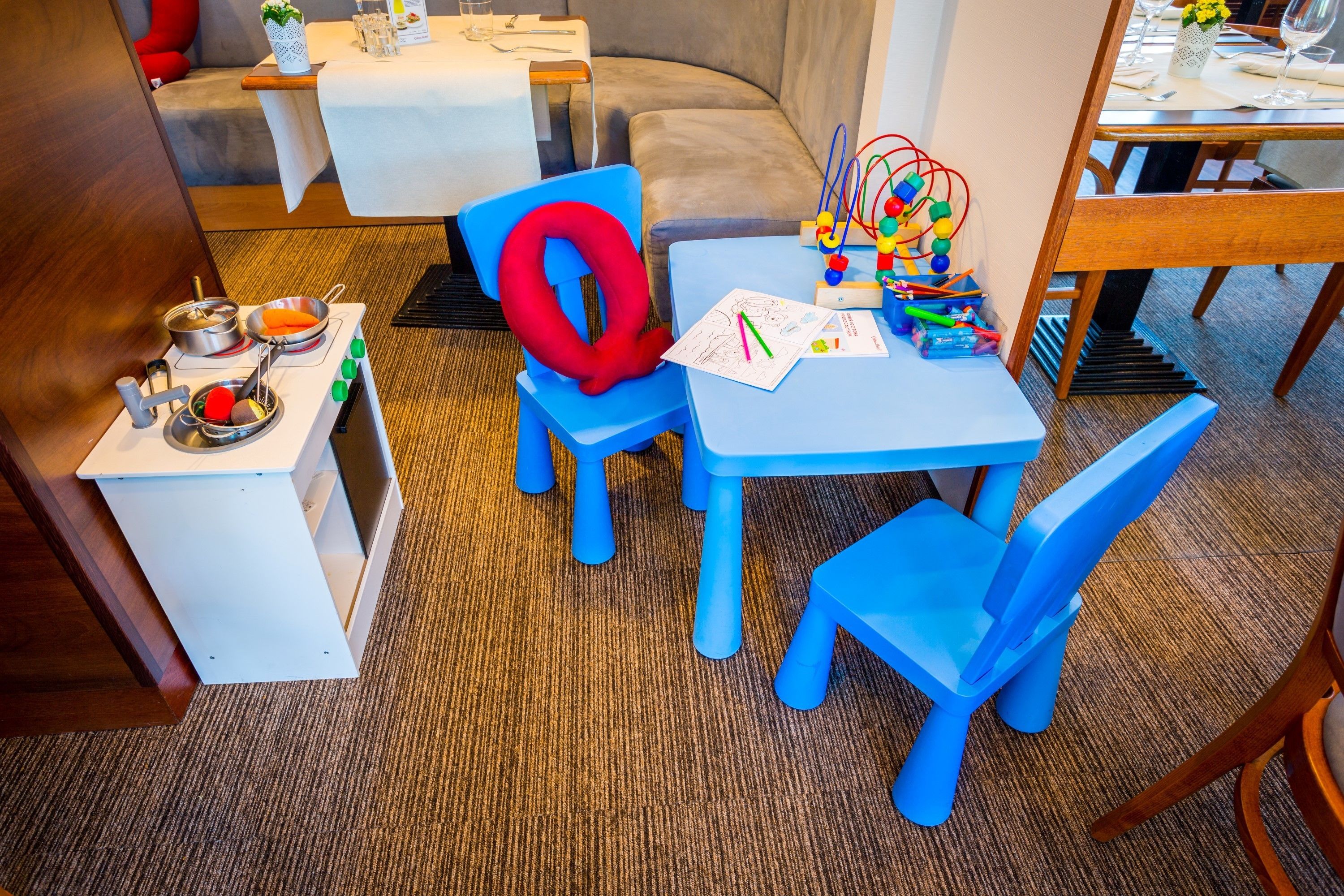 Un área de juegos infantiles con una silla azul, una mesa con juguetes y una letra 'O' roja en la pared.
