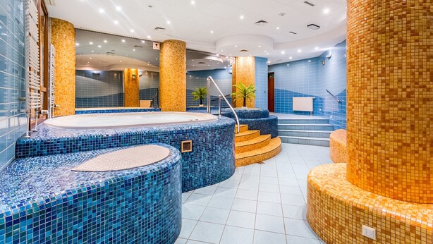 Moderni spa-alue, jossa on sinisen ja oranssin värisiä mosaiikkilaatoilla päällystettyjä porealtaita ja portaikko, joka johtaa ylemmälle tasolle.