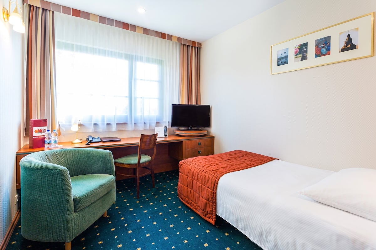 Une chambre d’hôtel avec un lit, un bureau avec un ordinateur, une chaise et un téléviseur.