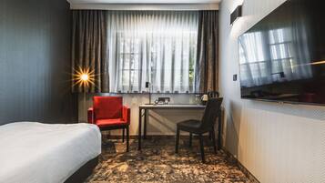 Una camera d'albergo con un letto, due sedie, una scrivania e un'ampia finestra con tende.