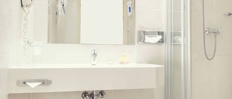 Un baño moderno con cabina de ducha de vidrio, un lavamanos blanco con un espejo encima y un inodoro con dispensador de toallas de papel.