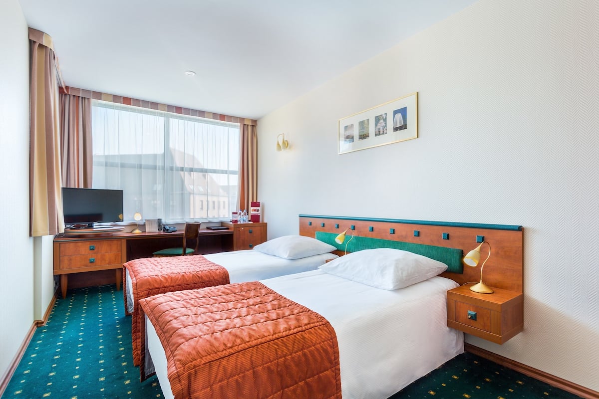 Une chambre d’hôtel avec deux lits, un bureau avec un ordinateur, une télévision et une fenêtre avec des rideaux.