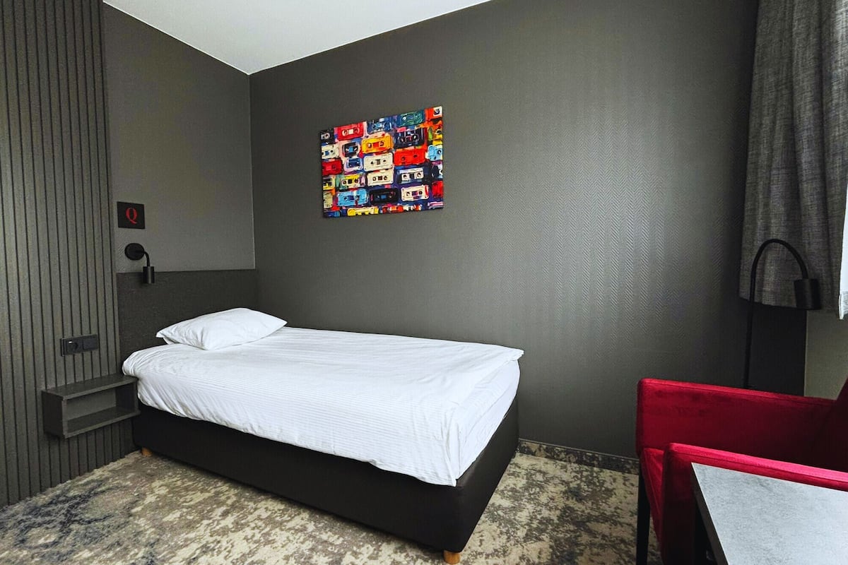Une chambre d’hôtel avec un lit, une chaise rouge, une œuvre d’art accrochée au mur, une table de chevet et une lampe.