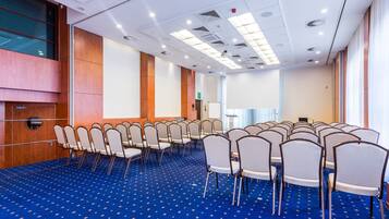 Ein Konferenzraum mit Reihen von Stühlen, einem blauen Teppich und einer weißen Decke mit Beleuchtung.