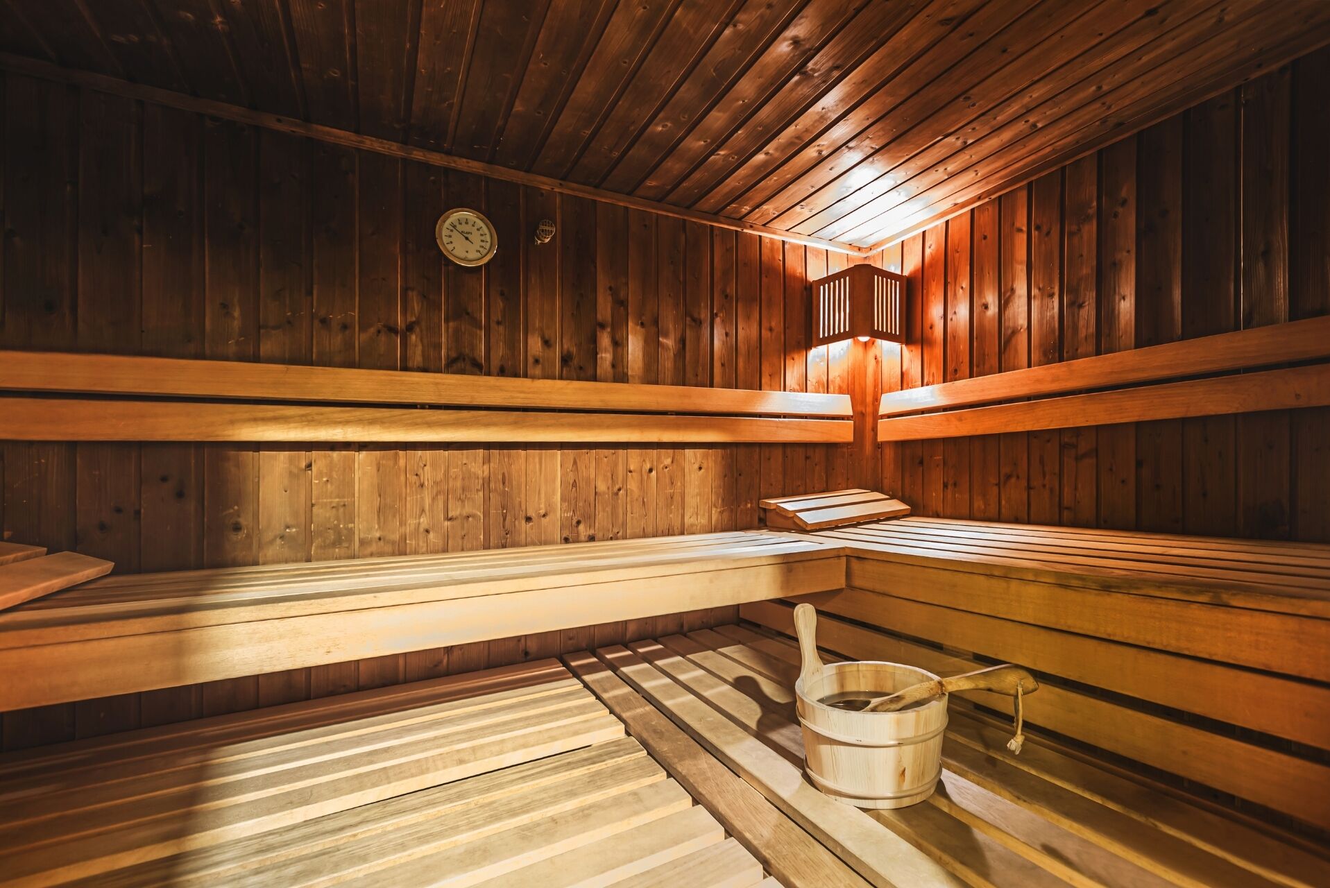 Un sauna avec des bancs en bois et un seau en bois accompagné d’une louche.