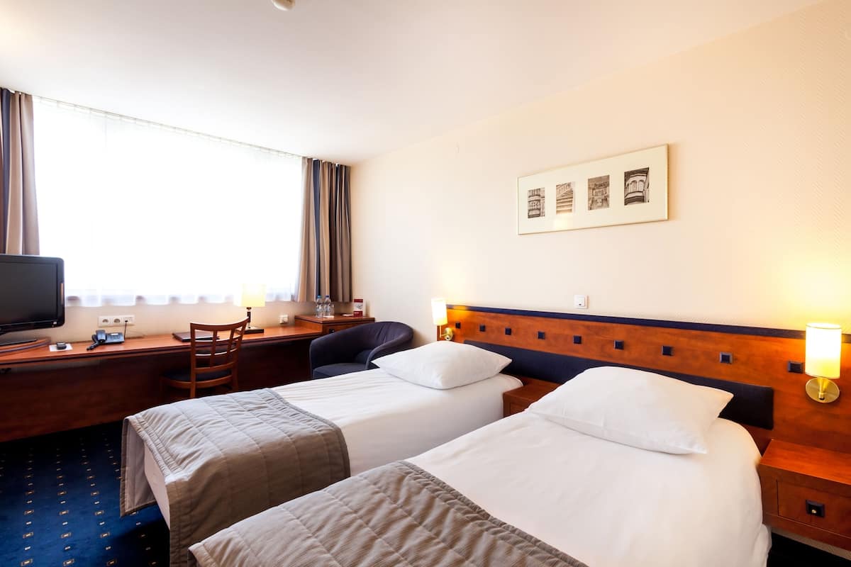 A hotel room with two beds, a desk with a computer, a chair, and a TV.
