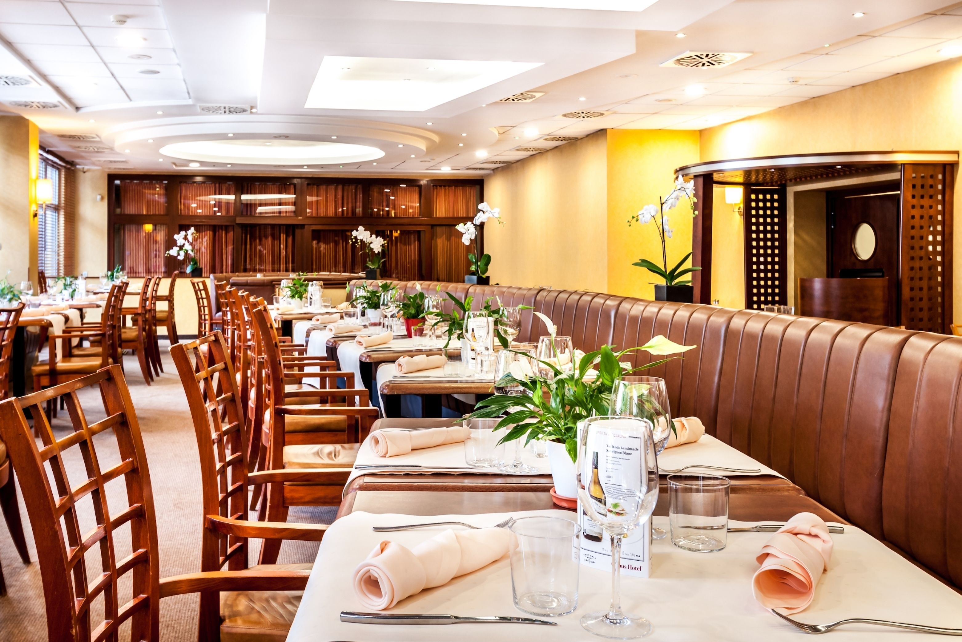 Un restaurante con cabinas de madera, mesas dispuestas con manteles blancos y plantas en macetas.