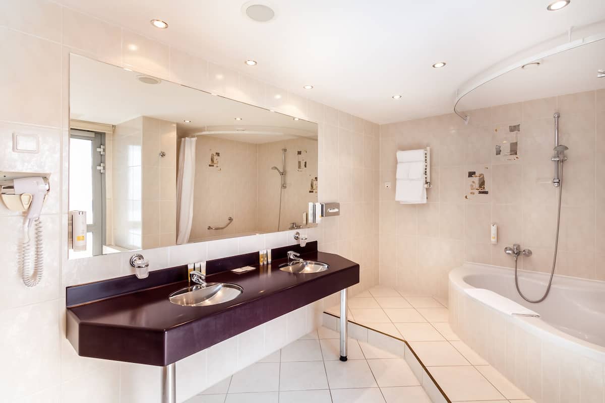 A modern bathroom with a dark countertop, two sinks, a large mirror, and a separate shower area.