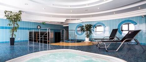 Una amplia piscina cubierta con un jacuzzi, rodeada de paredes con azulejos azules y un diseño de techo circular.