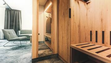 Habitación de hotel moderna con un revestimiento de madera, una zona de estar con una silla y un sofá, y un banco empotrado con espacios de almacenamiento.