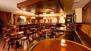 A bar area with multiple wooden tables and chairs, a bar counter, and a large wooden ceiling structure.