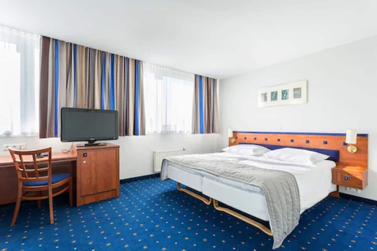 A hotel room with a bed, a desk with a computer, a chair, and a television.