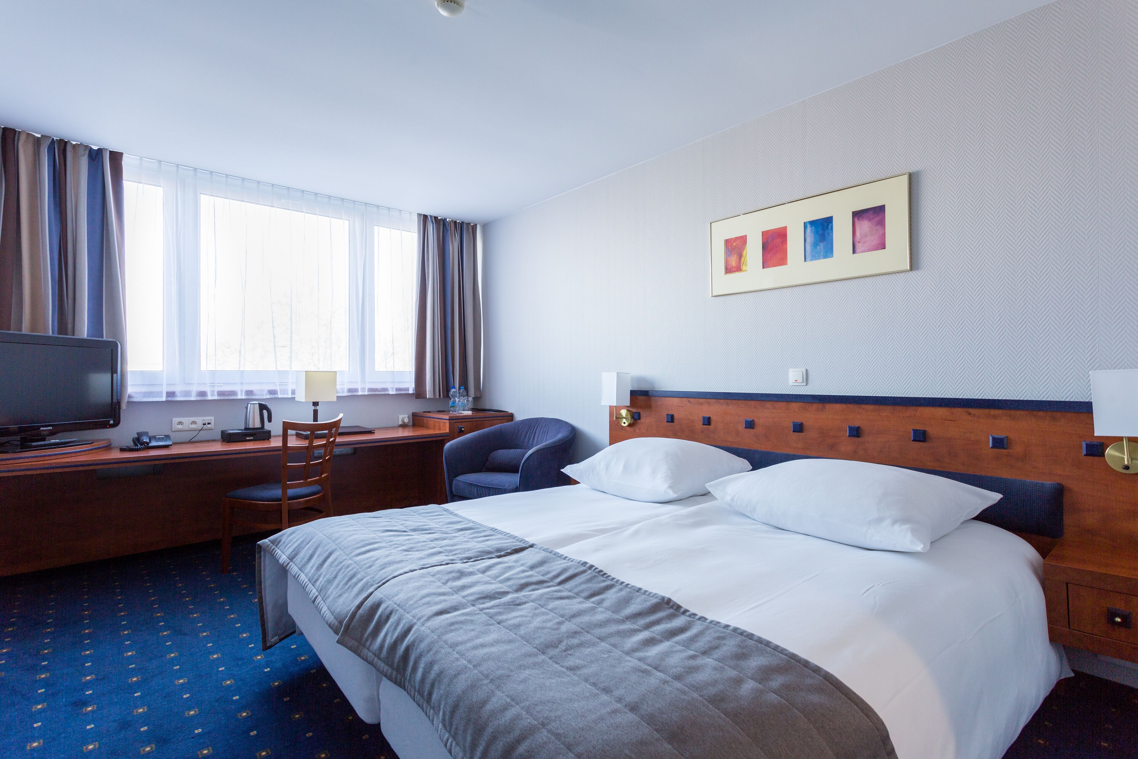 A hotel room with a bed, a desk with a computer, a chair, and a television.