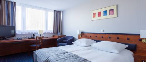 A hotel room with a bed, a desk with a computer, a chair, and a television.