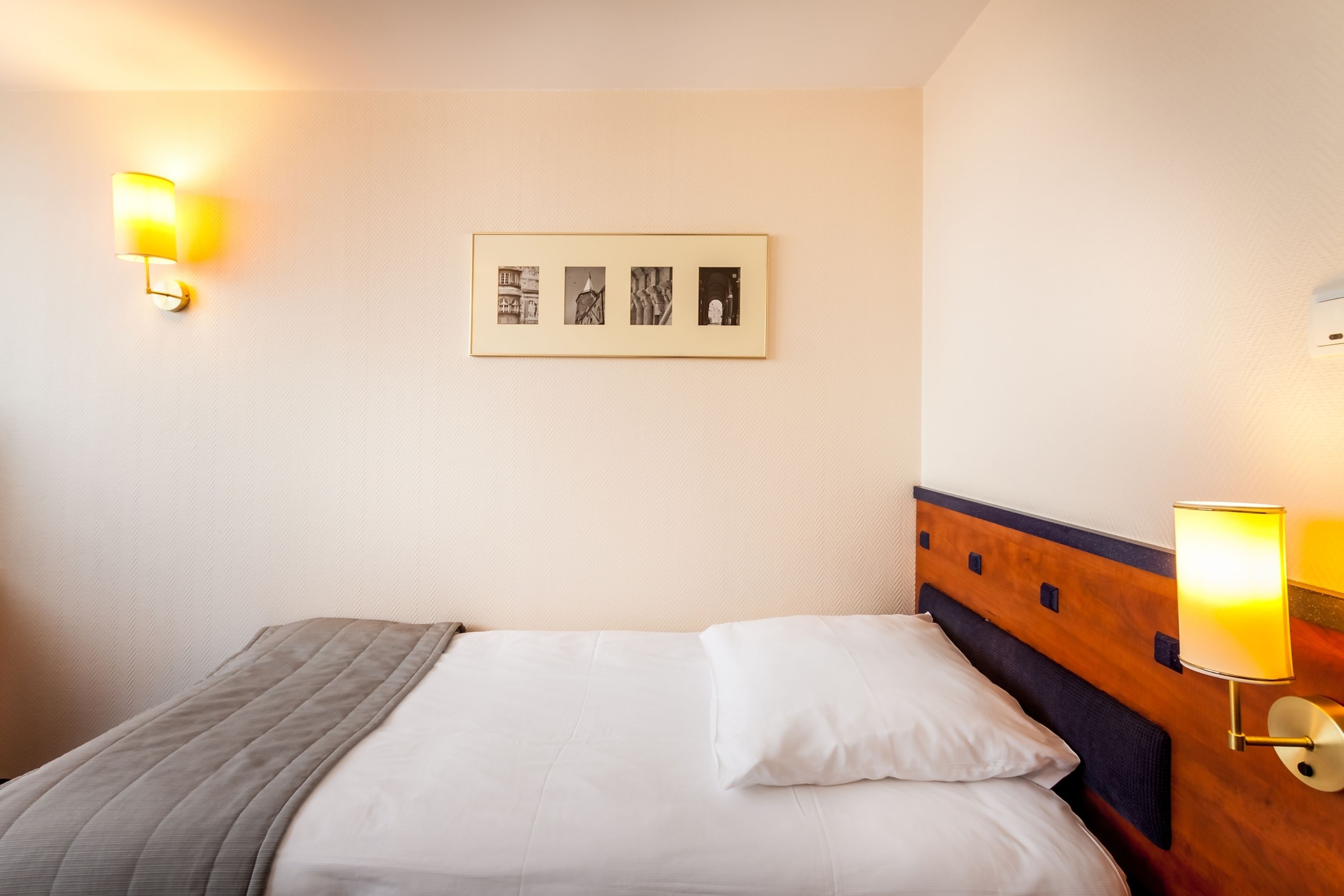 Una cama bien hecha con un cabecero, dos lámparas de pared y un cuadro en la pared.