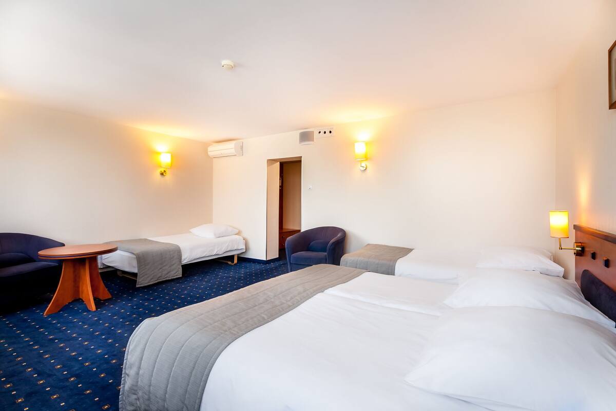 A hotel room with two single beds, a sofa, a small table, and two wall-mounted lamps.