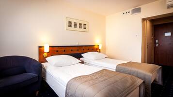 A hotel room with two single beds, a wooden headboard, a wall-mounted picture, a desk with a chair, and a door with a handle.