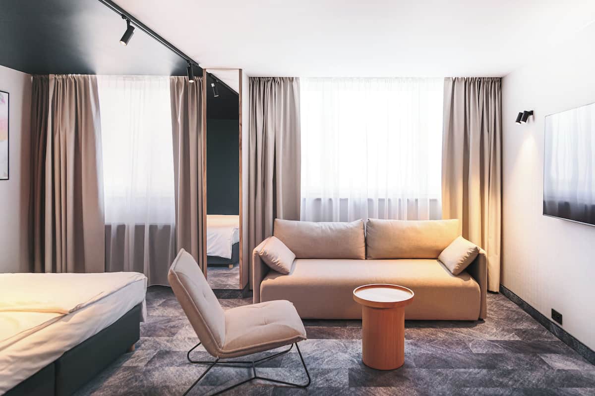 A modern hotel room with a bed, a sofa, a chair, and a small table.