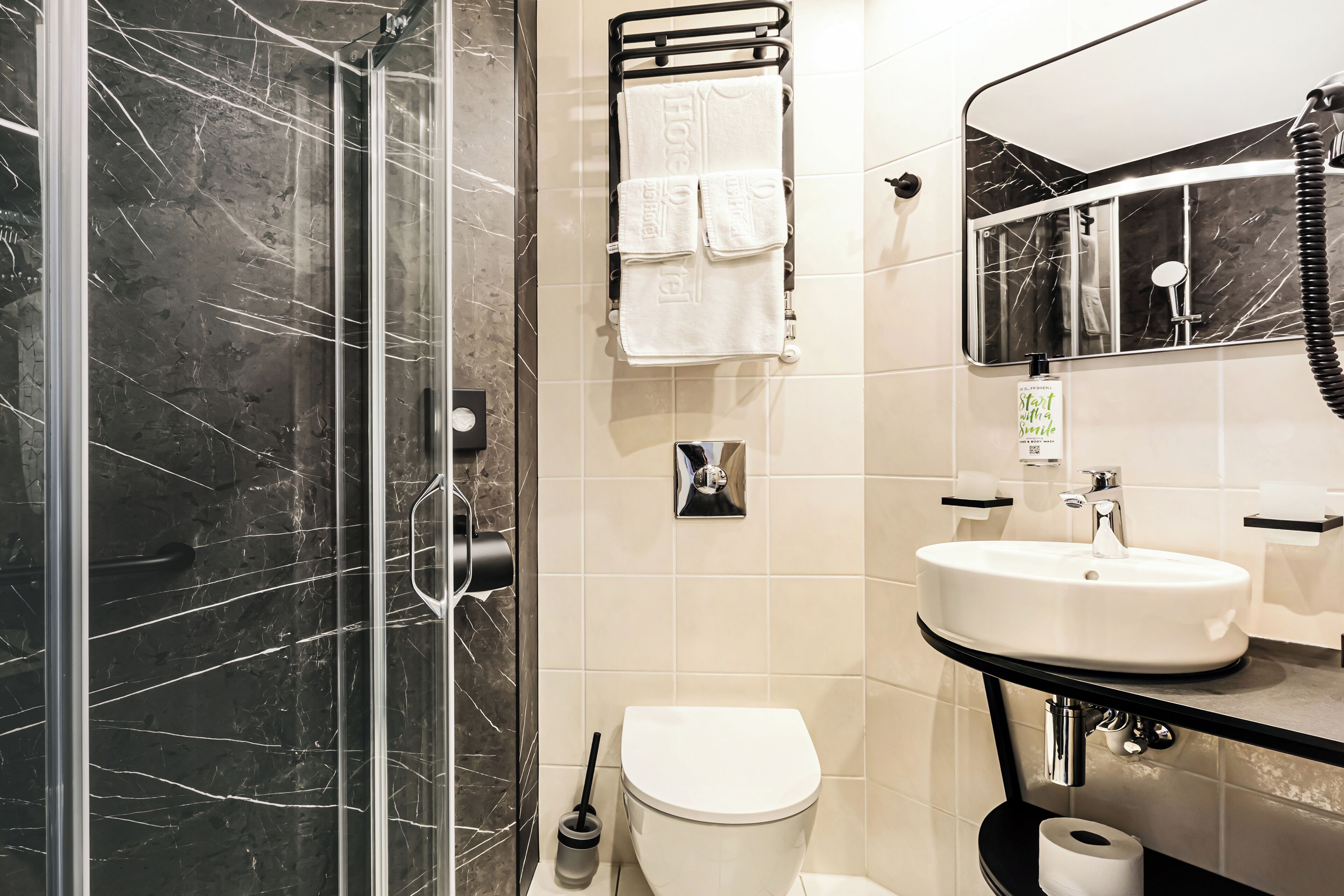 Ein modernes Badezimmer mit einer Duschkabine aus Glas, einer weißen Toilette, einem Waschbecken mit Spiegel und einem Handtuchhalter mit weißen Handtüchern.