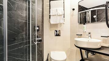 A modern bathroom with a glass shower enclosure, a white toilet, a sink with a mirror above it, and a towel rack with white towels.