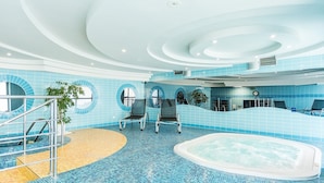 An indoor swimming pool with a tiled floor, a hot tub, and seating areas.