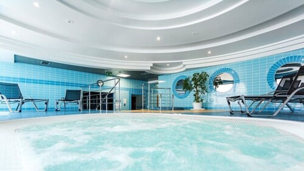 An indoor swimming pool with a circular design, blue tiled walls, and lounge chairs around the perimeter.