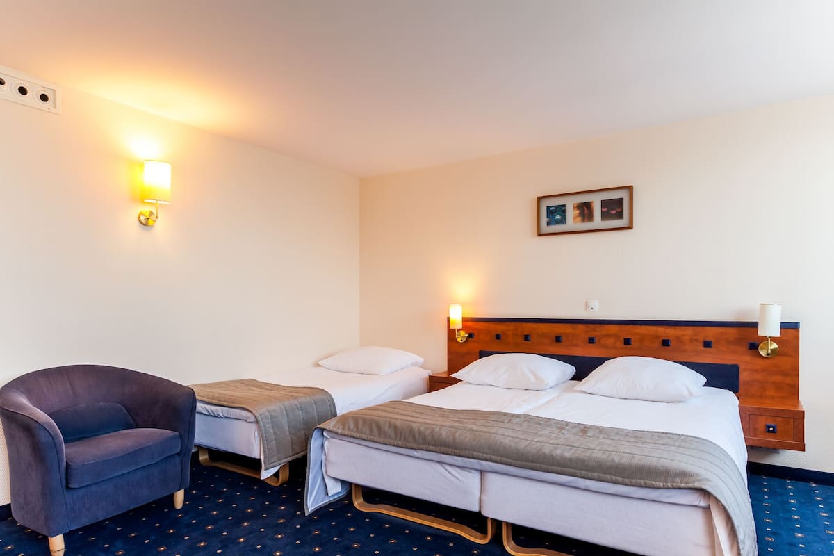 A hotel room with two single beds, a chair, and a nightstand with a lamp.
