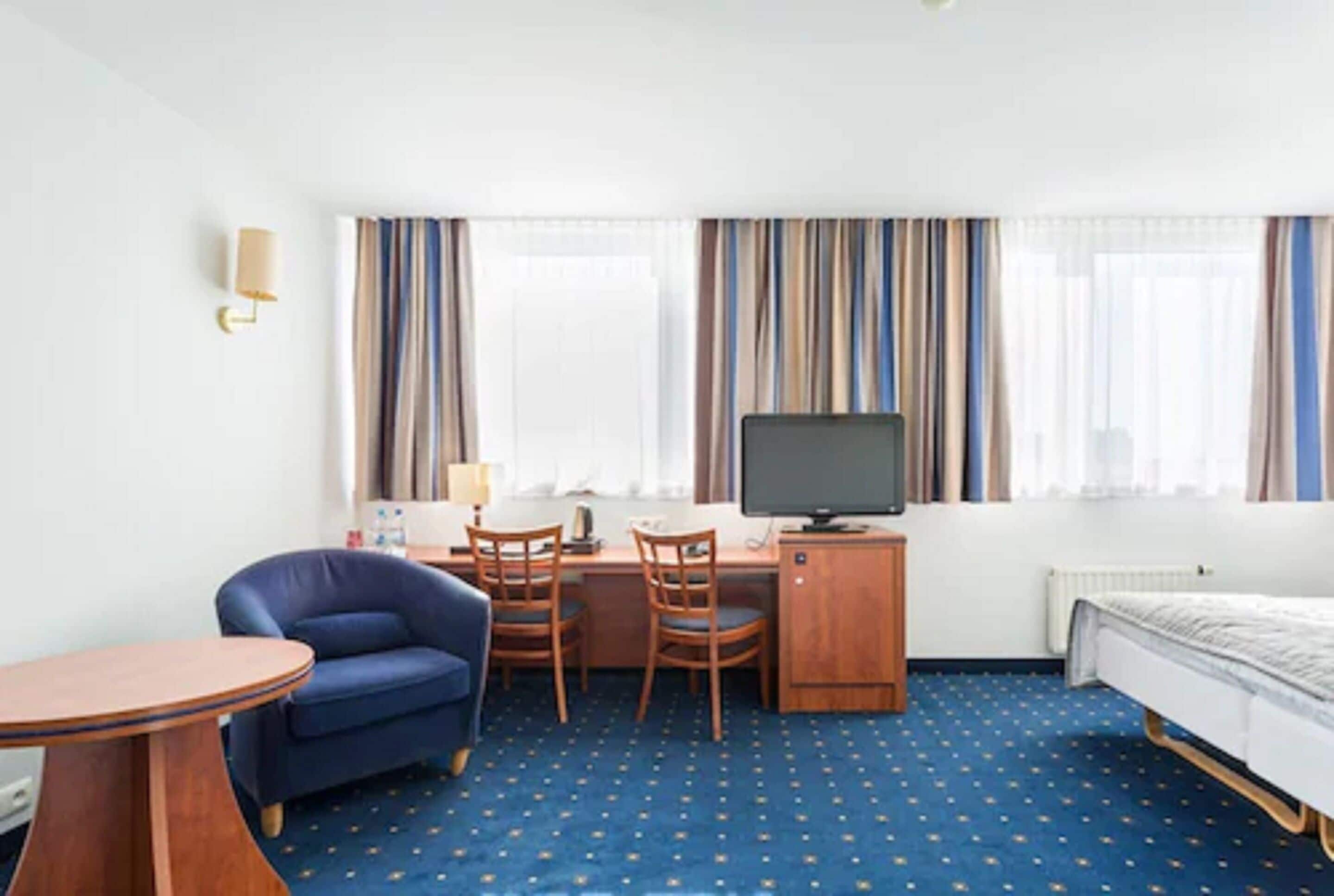 Une chambre d’hôtel comprenant un lit, un bureau avec un ordinateur, une chaise, une petite table et un téléviseur.