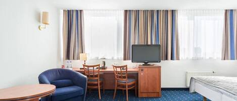 Une chambre d’hôtel comprenant un lit, un bureau avec un ordinateur, une chaise, une petite table et un téléviseur.