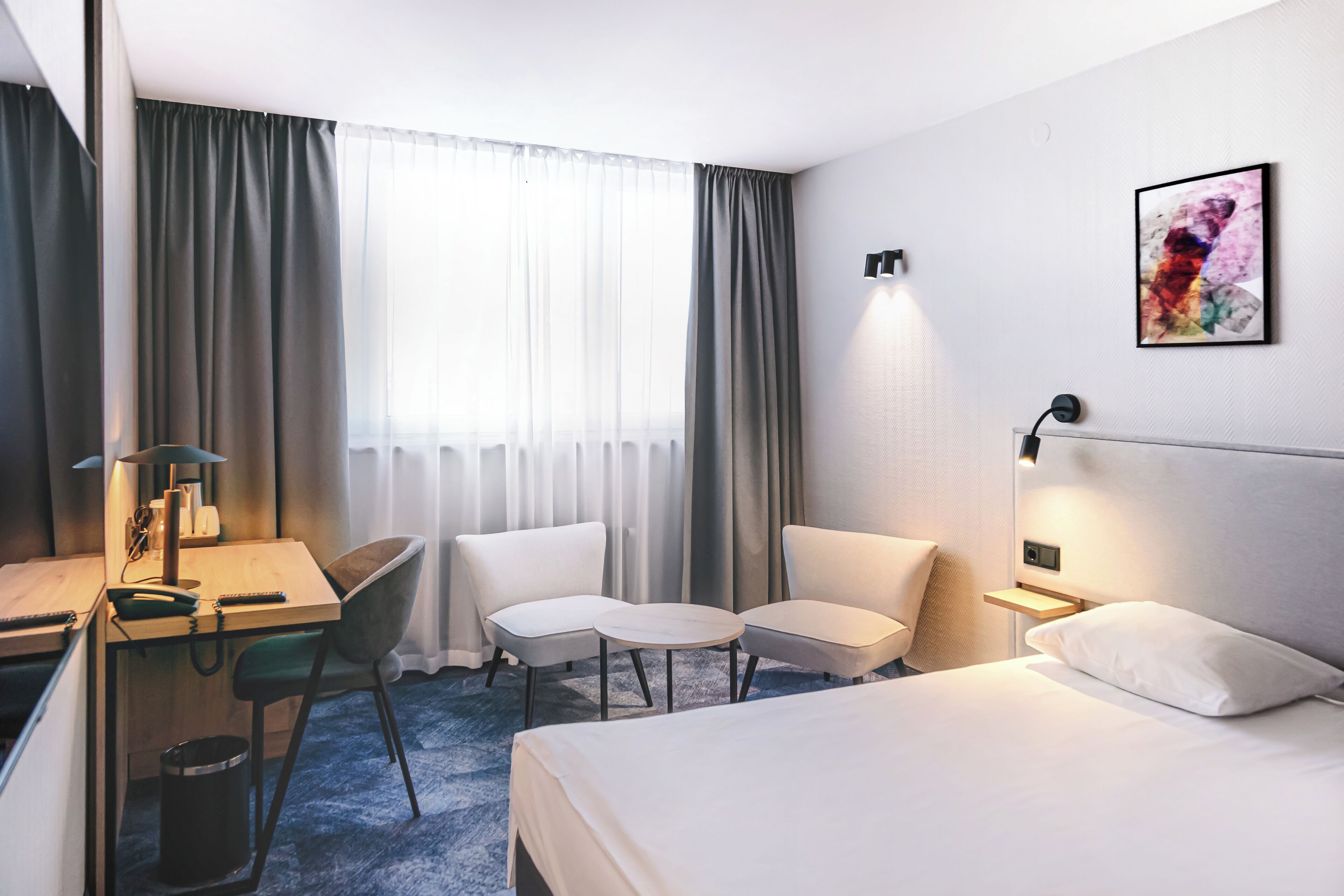 Ein Hotelzimmer mit Bett, Schreibtisch, zwei Stühlen, einem kleinen Tisch und einem Bild an der Wand.