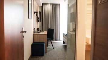 Una habitación de hotel con escritorio, silla y un pequeño reposapiés.