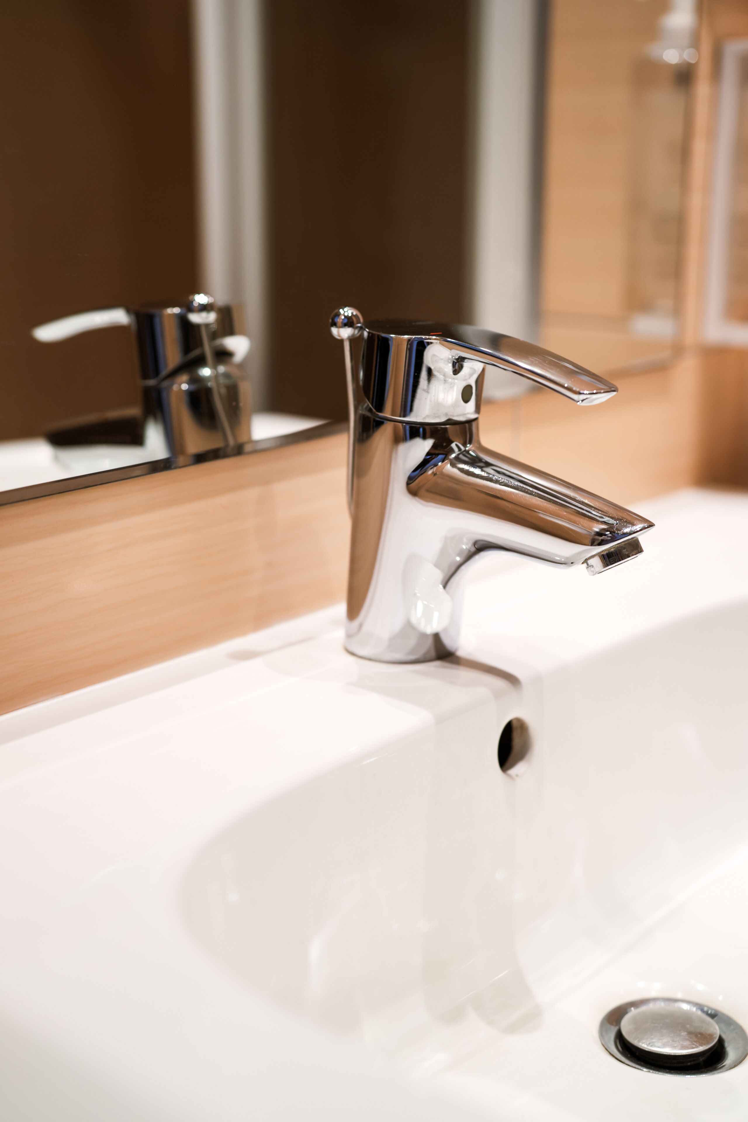 A chrome faucet with a single handle and a side lever, mounted on a white sink with a drain hole.