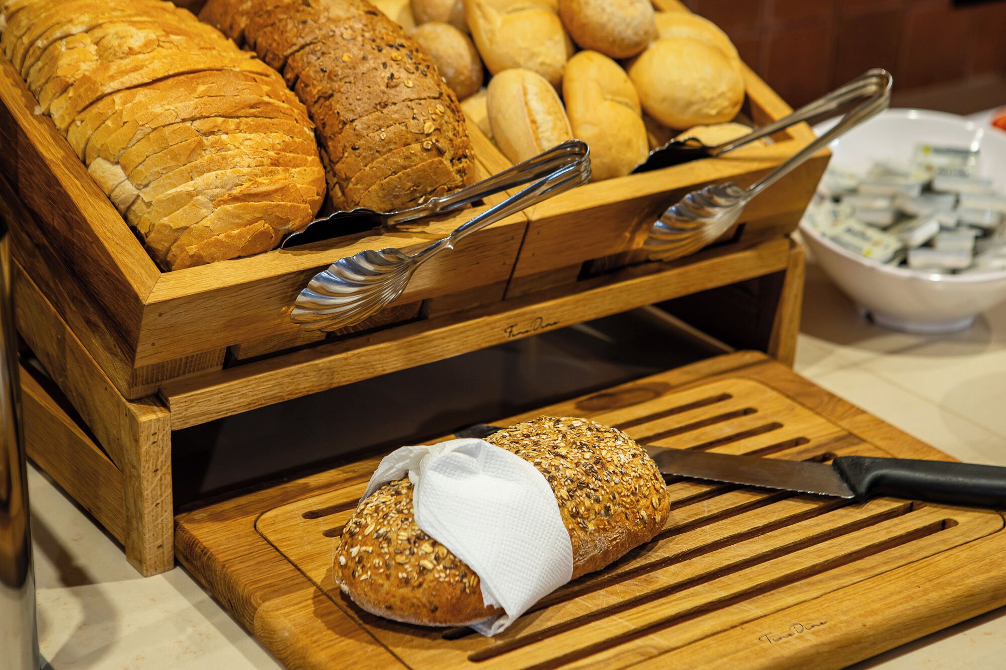 Eine Holzbrotpräsentation mit verschiedenen Brotsorten und einem Messer auf einem Schneidebrett.