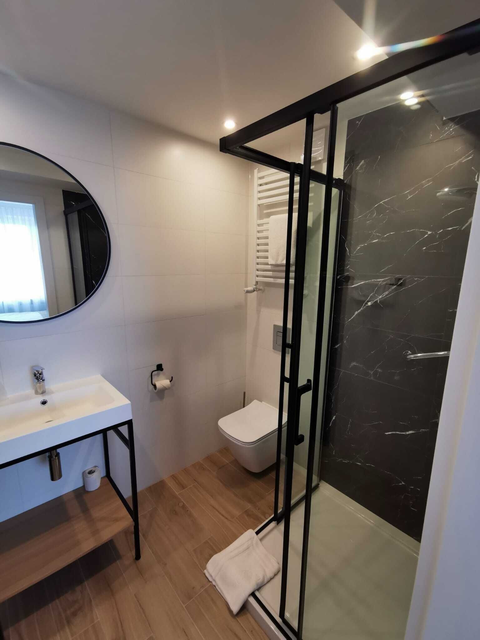 A modern bathroom with a white sink, toilet, and glass shower enclosure.