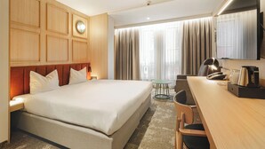 A hotel room with a large bed, a desk, a chair, a small table, a clock, and a television.