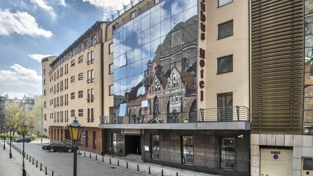A hotel with a large glass facade reflecting the sky and a building behind it.