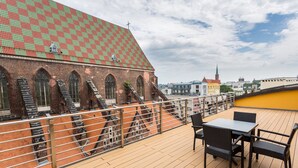 A rooftop terrace with a view of a historic building with a checkered roof, a staircase, and a table with chairs.