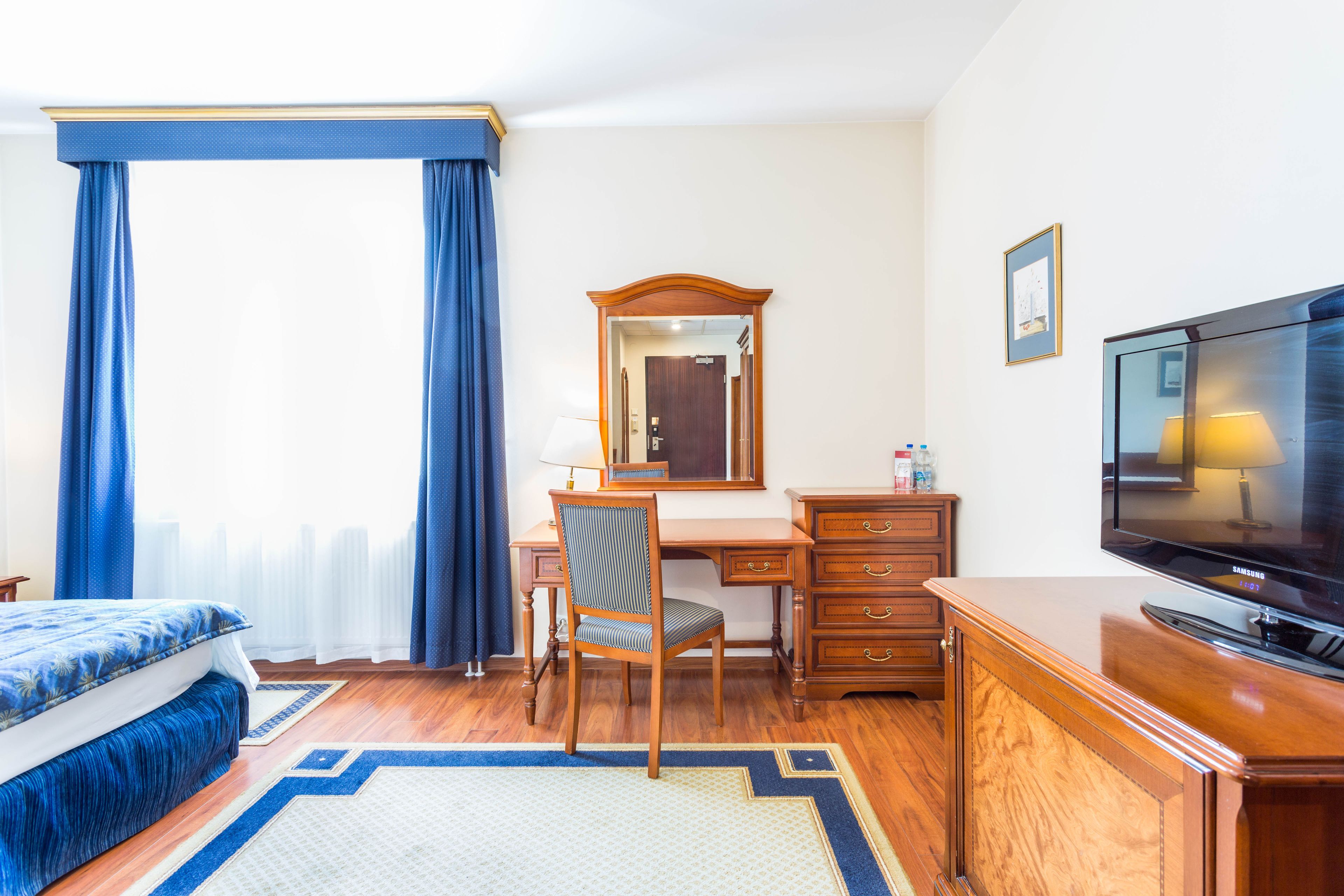 A hotel room with a bed, a desk, a chair, a television, and a dresser.