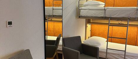 A hotel room with bunk beds, a mirror, two chairs, and a carpeted floor.