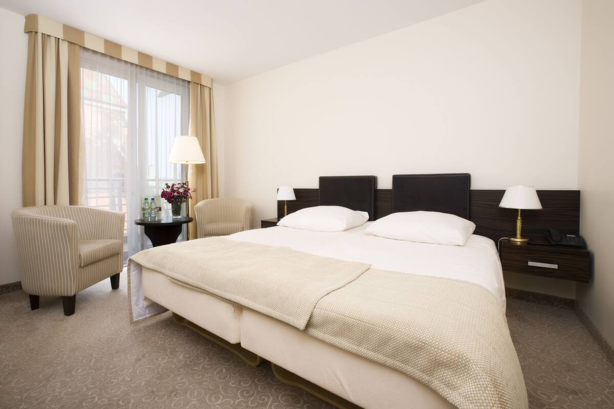 A hotel room with a large bed, two bedside tables with lamps, a chair, and a window with curtains.