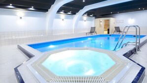 An indoor swimming pool with a hot tub, seating area, and a door leading to a changing room.
