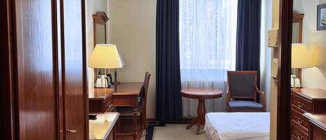 Una habitación de hotel con cama, escritorio, silla, mesa y lámpara.