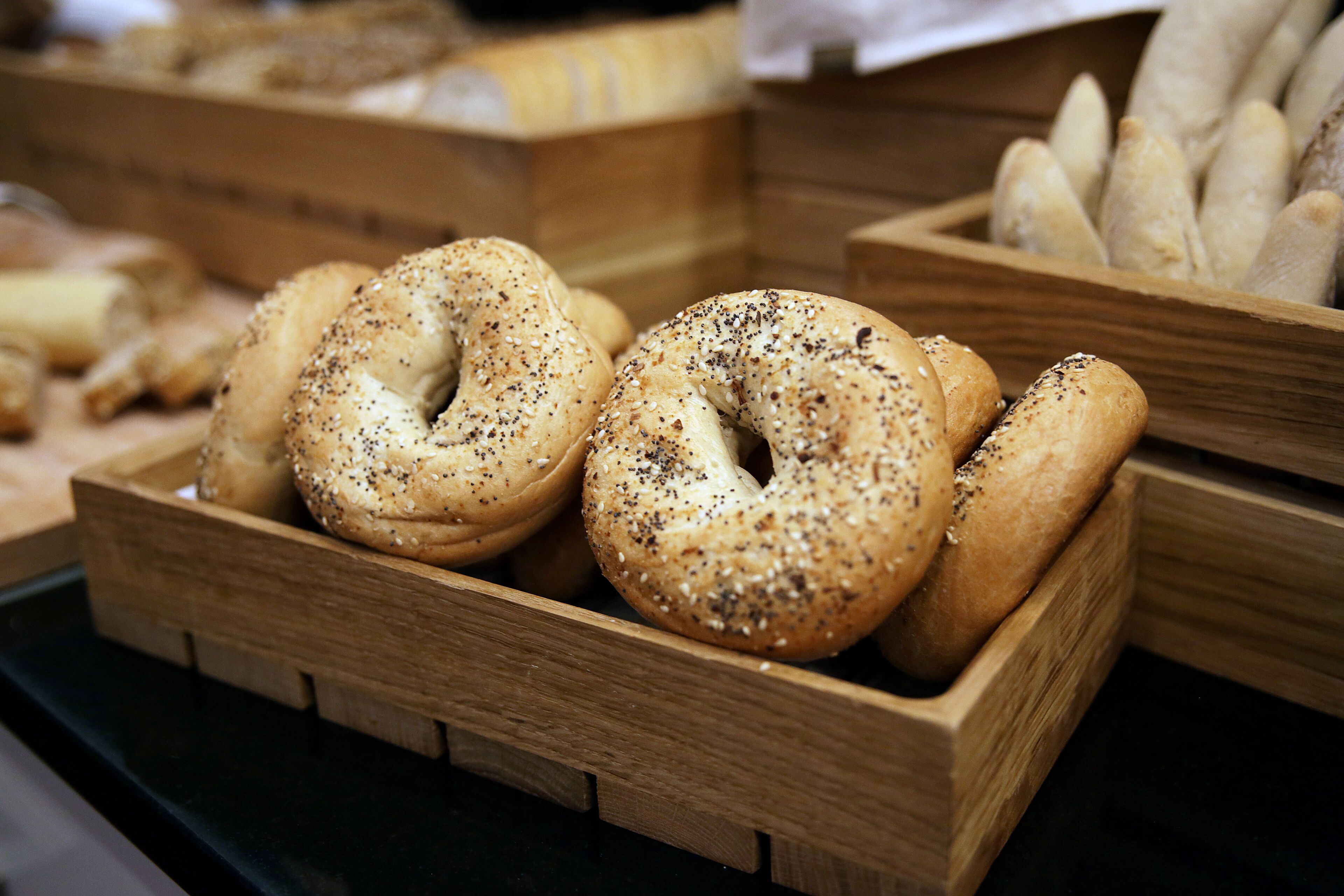 A wooden display case containing bagels with sesame seeds and poppy seeds.