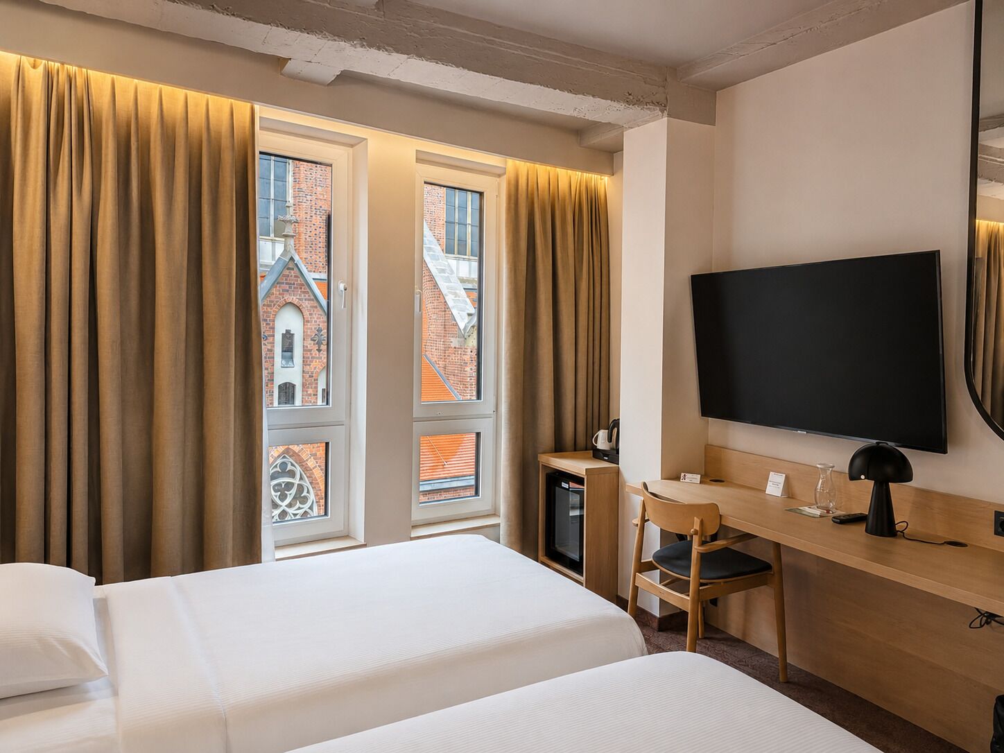Habitación de hotel con dos camas, un escritorio, televisor y vistas a un edificio de ladrillo.