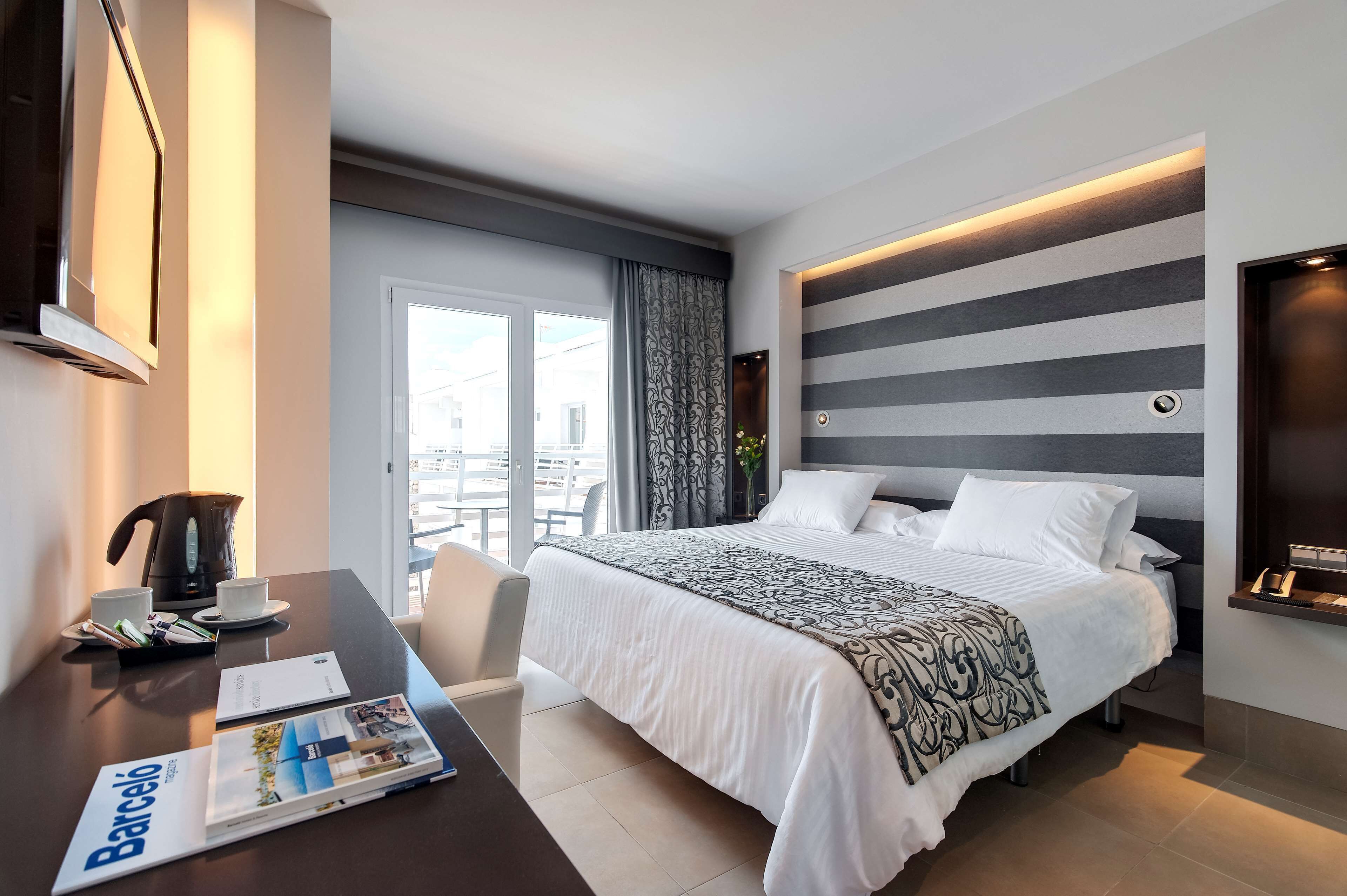 A modern hotel room with a large bed, a desk with a coffee maker, and a magazine on the table.