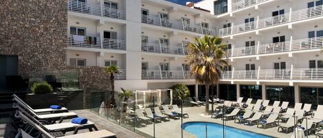 A hotel with a pool area, lounge chairs, and a stone wall.