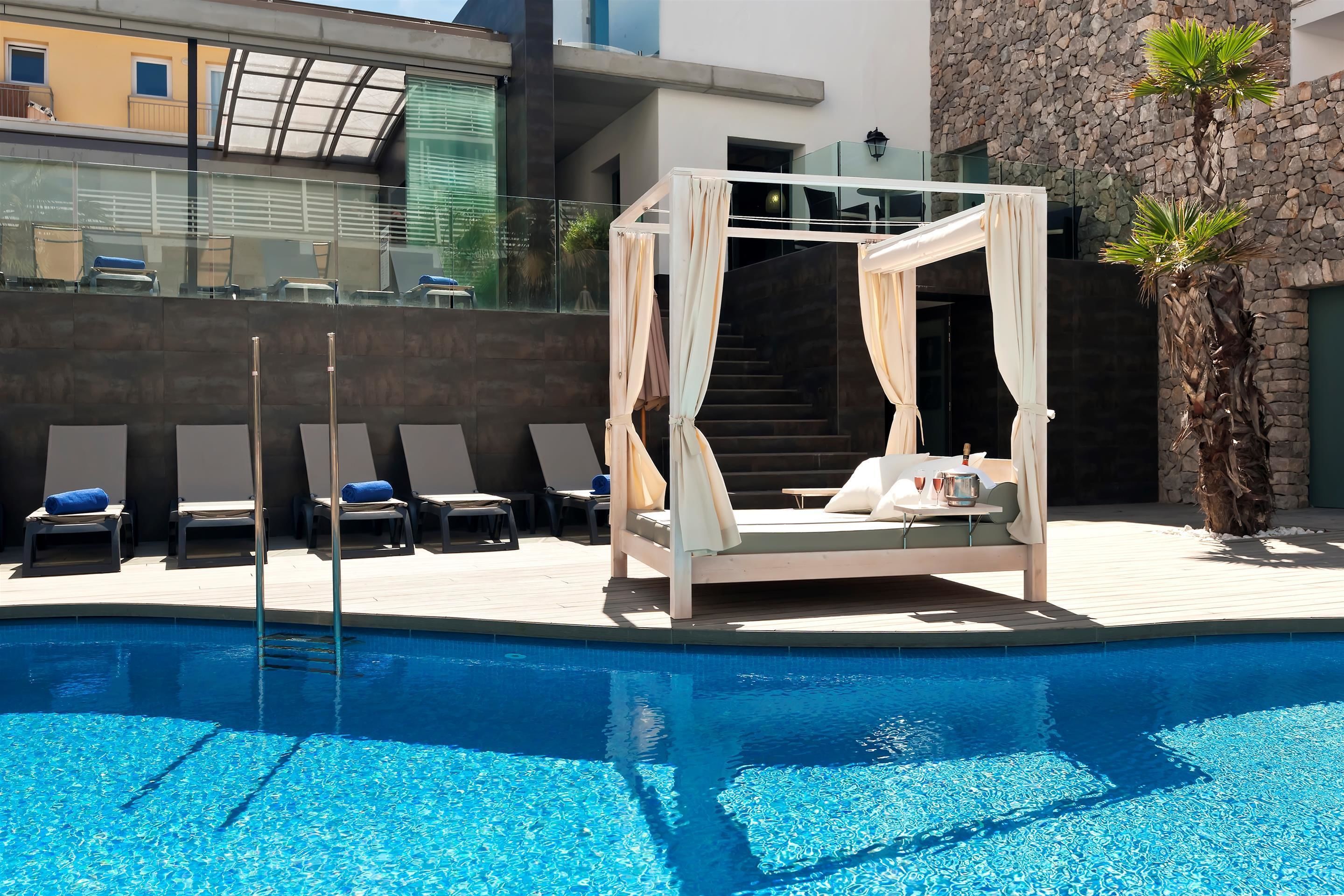 A poolside area with a canopy bed, lounge chairs, and a palm tree.
