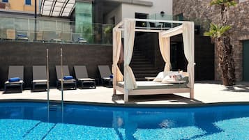A poolside area with a canopy bed, lounge chairs, and a palm tree.