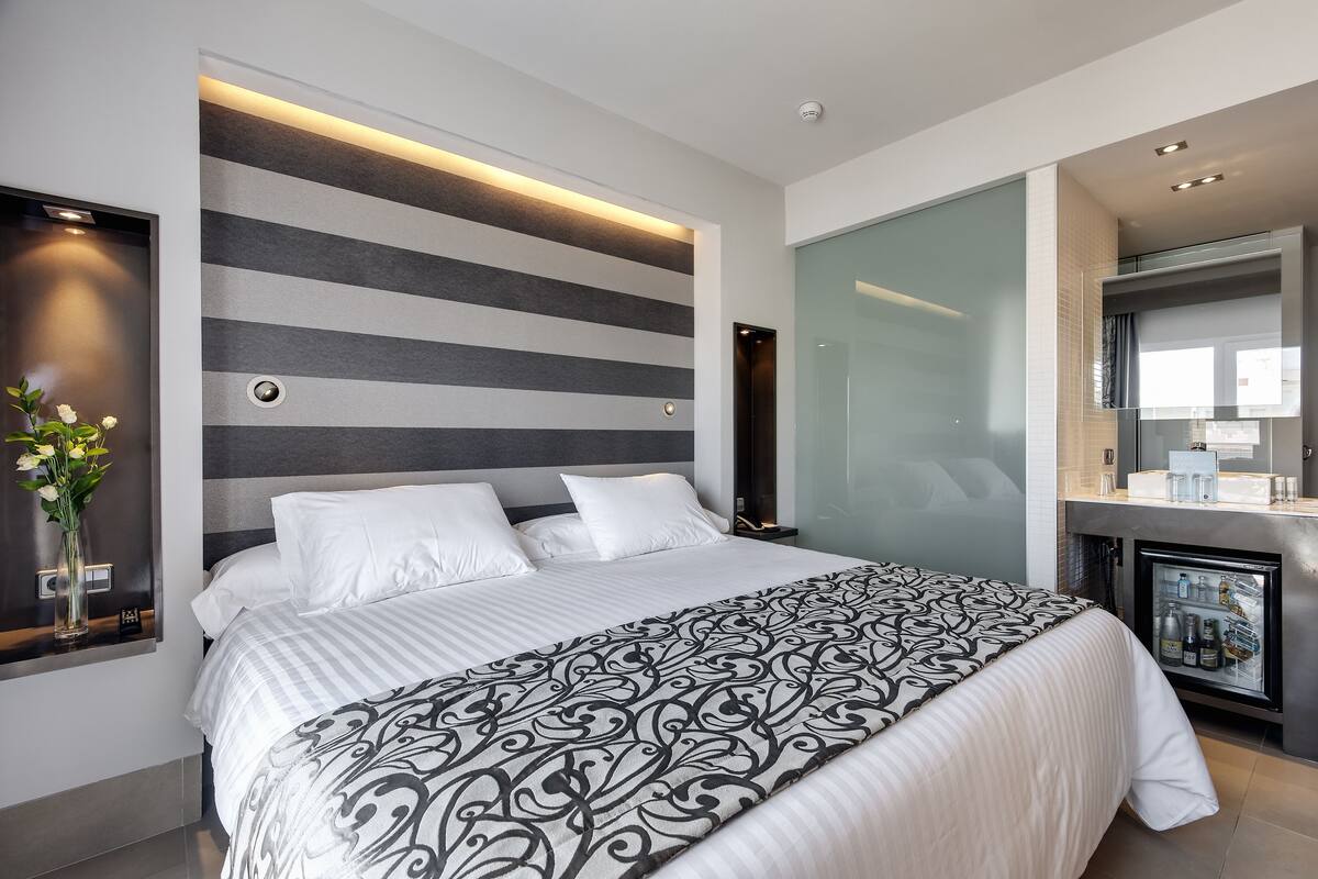 Une chambre d’hôtel moderne dotée d’un grand lit, d’un mini-réfrigérateur intégré et d’un décor mural élégant à rayures.
